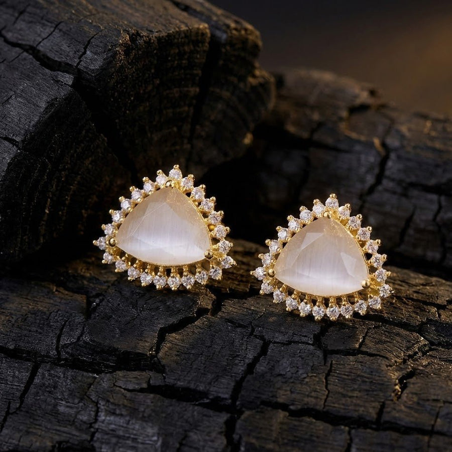 Pairs of milky white trillion cut gemstone halo studs placed on soft cream fabric