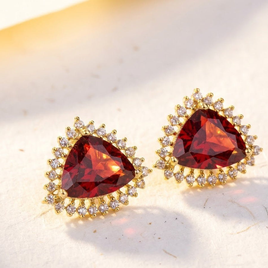 Close-up of deep red trillion cut gemstone stud earrings with clear stone halo on soft light surface