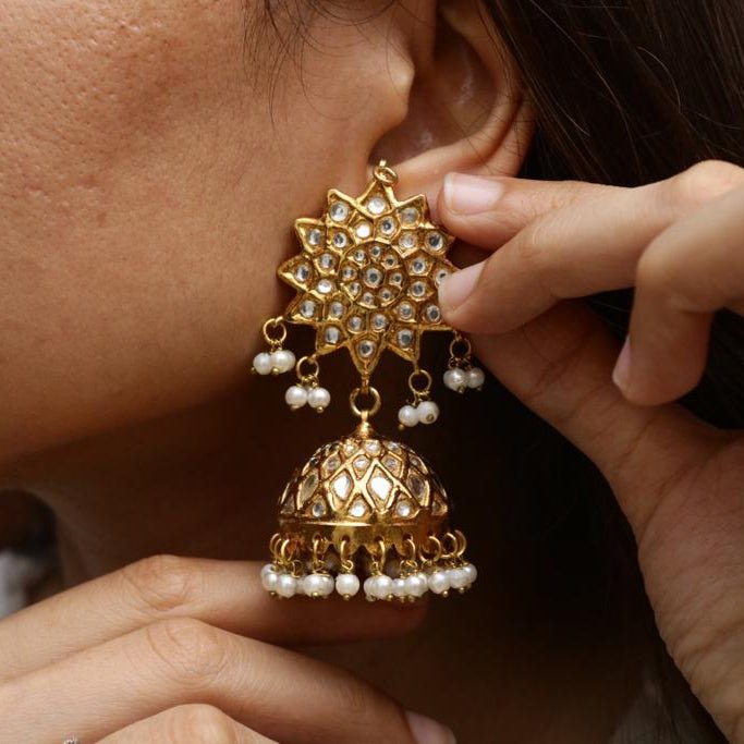 Close-up of a woman wearing gold-plated jhumka earring with floral stone motif and dangling pearls, highlighting the intricate craftsmanship