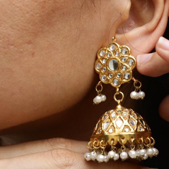 Close-up of a woman’s ear showcasing gold Jhumka earring with intricate stone detailing and pearl drops