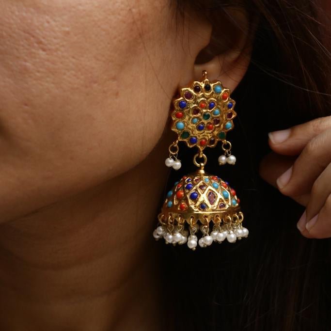 Close-up of a woman wearing a gold plated Jhumka earring decorated with colorful stones and pearl dangles, showcasing the intricate traditional design