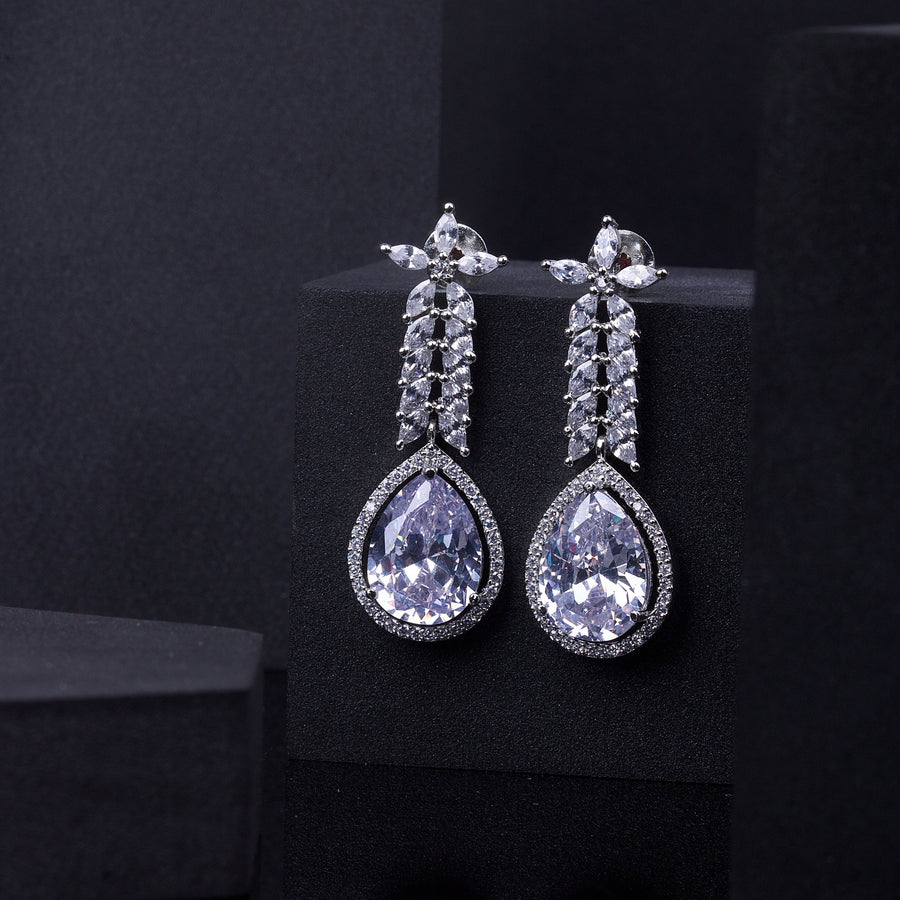 Pair of elegant pear-shaped zircon drop earrings with rhodium plating displayed on a black stand
