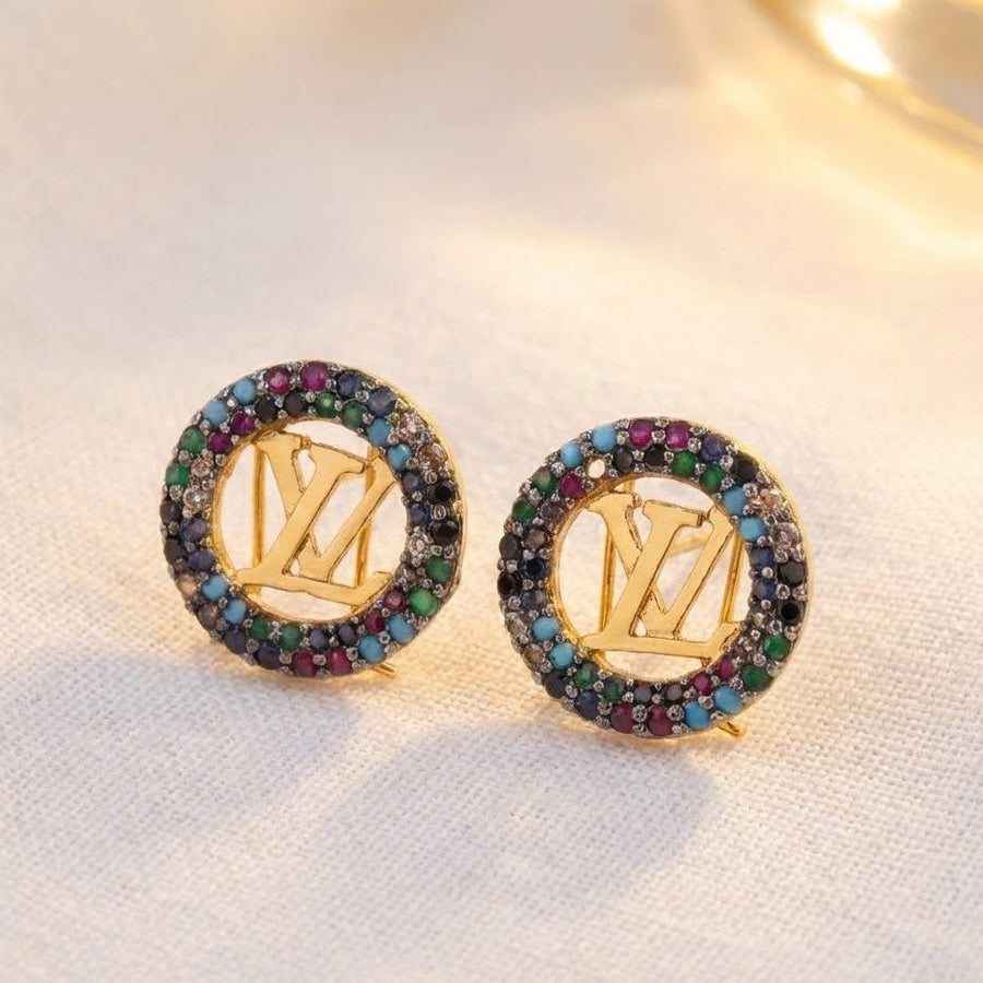 Gold-tone round earrings with multicolor stones placed on a light fabric background under soft lighting