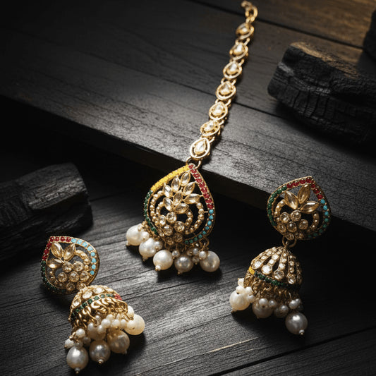 Close-up of Majesty Pearl Drop earrings and matching maang tikka with multicolored stones and pearl accents on dark wood surface
