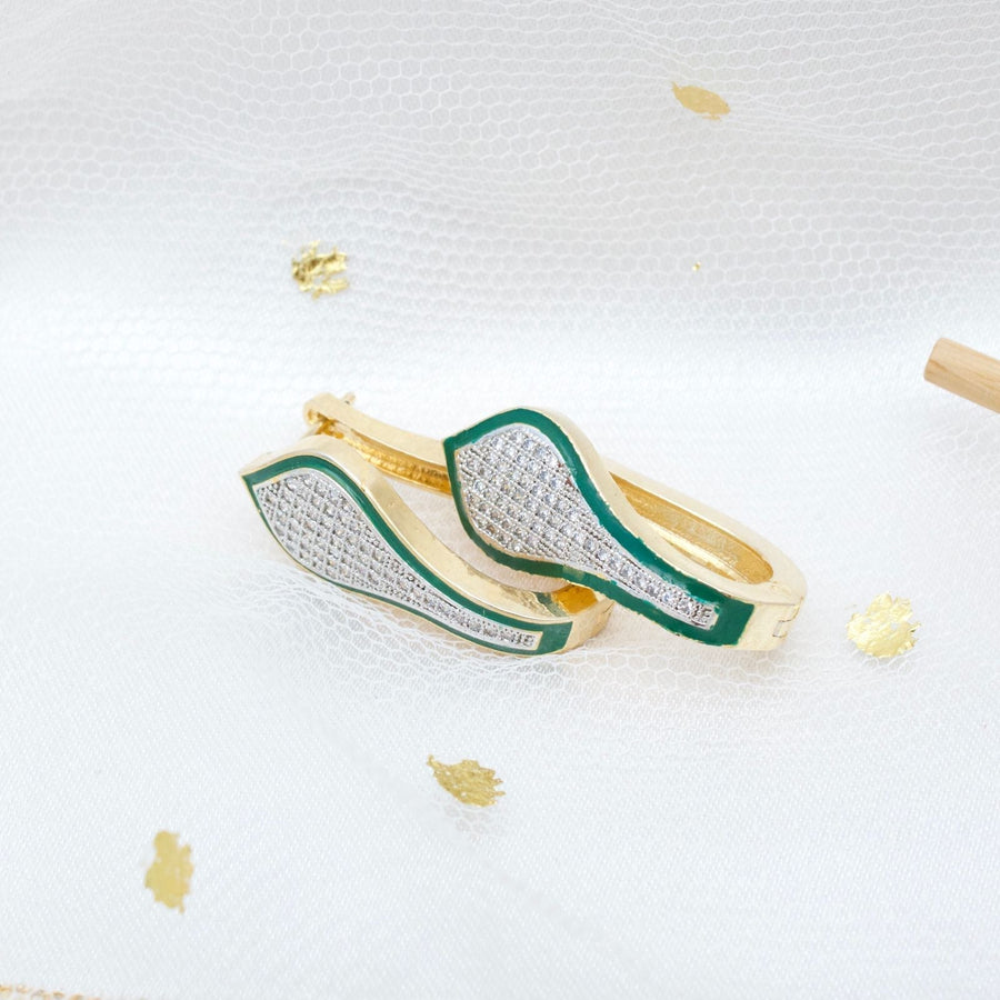 Gold tone hoop earrings with green enamel and pavé stones laid on white sheer fabric with gold accents
