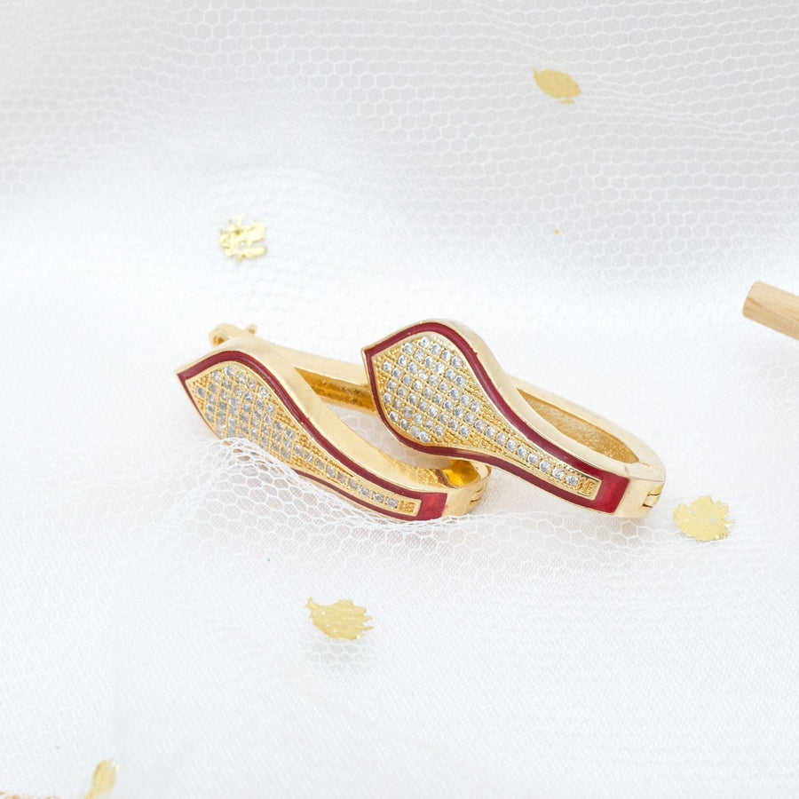 Gold tone hoop earrings with red enamel and pavé stones laid on white sheer fabric with gold accents