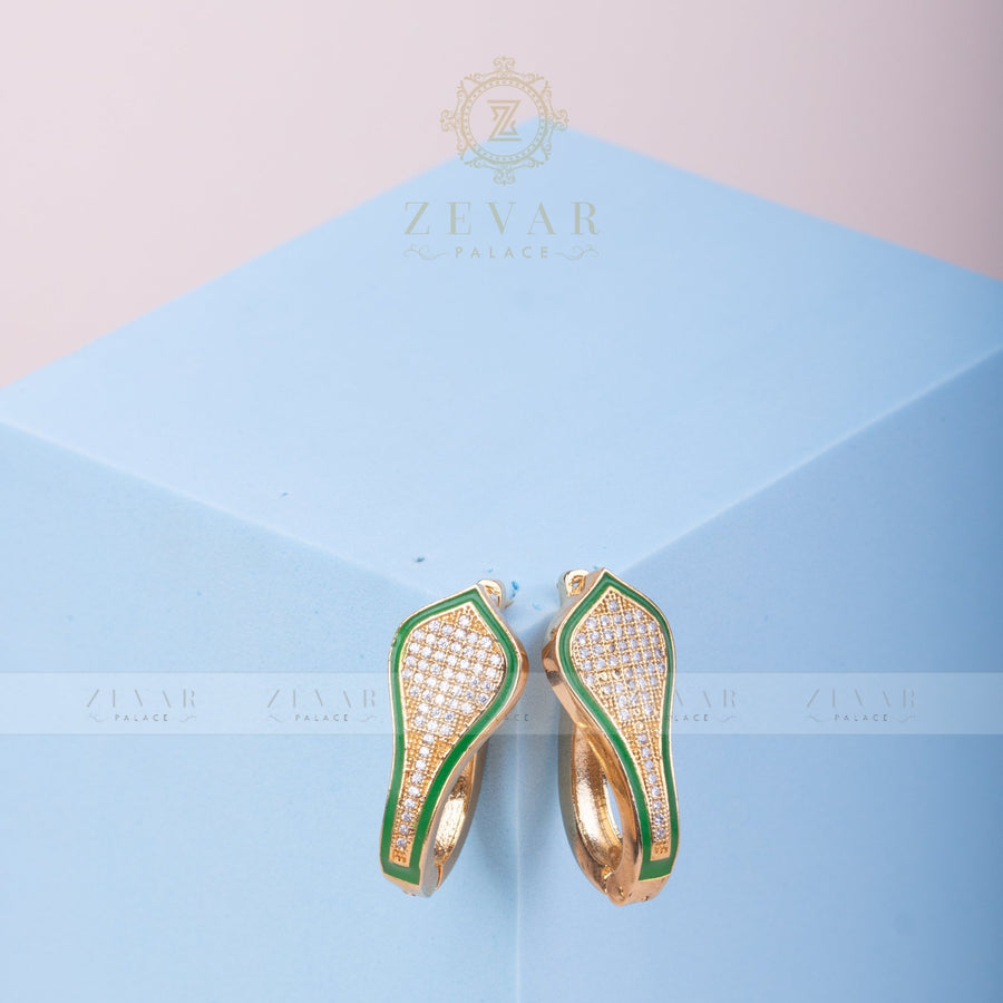 Close-up of green enamel bordered gold tone teardrop hoop earrings with pavé stones on light blue geometric stand
