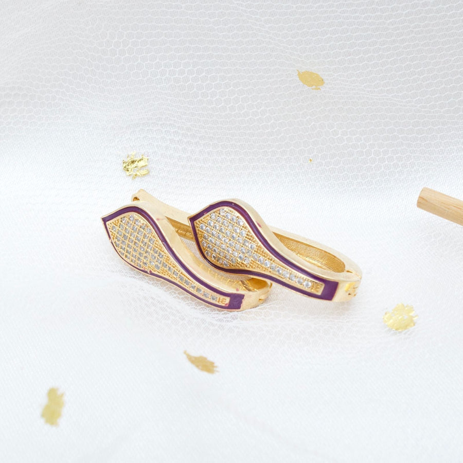 Gold tone hoop earrings with purple enamel and pavé stones laid on white sheer fabric with gold accents