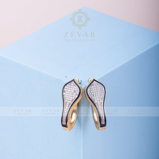 Pair of gold tone teardrop-shaped hoop earrings with black enamel border and pavé stone detailing displayed on light blue geometric stand