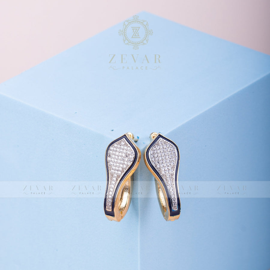 Pair of gold tone teardrop-shaped hoop earrings with black enamel border and pavé stone detailing displayed on light blue geometric stand