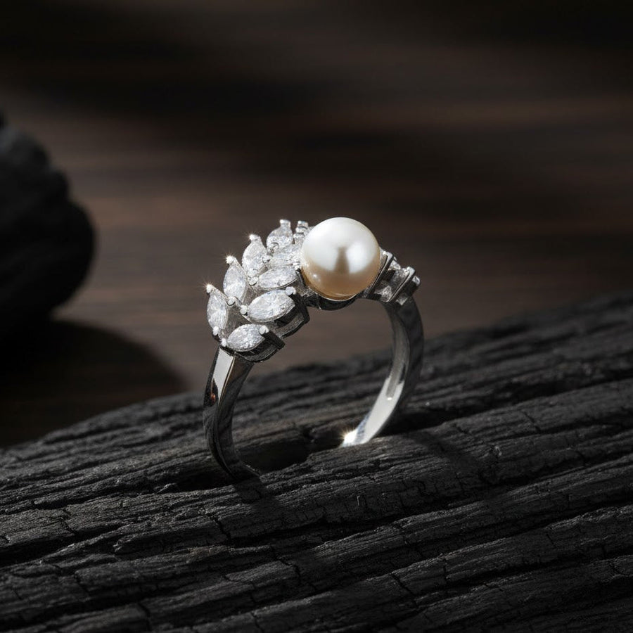 Close-up of a silver pearl and zirconia leaf design ring placed on textured dark wood, highlighting the stone sparkle and pearl luster.
