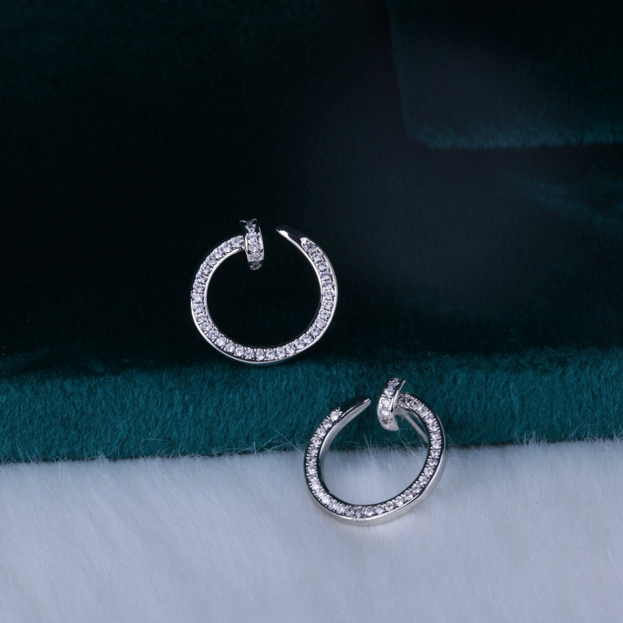 Silver-tone sparkling rhinestone circle hoop earrings placed on white surface with teal velvet background