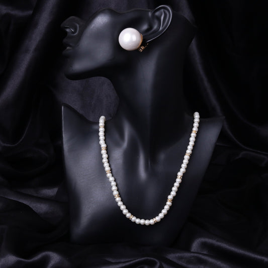 Black mannequin bust displaying a white mother of pearl necklace with gold-tone spacers and matching clip-on earring on a black satin background.