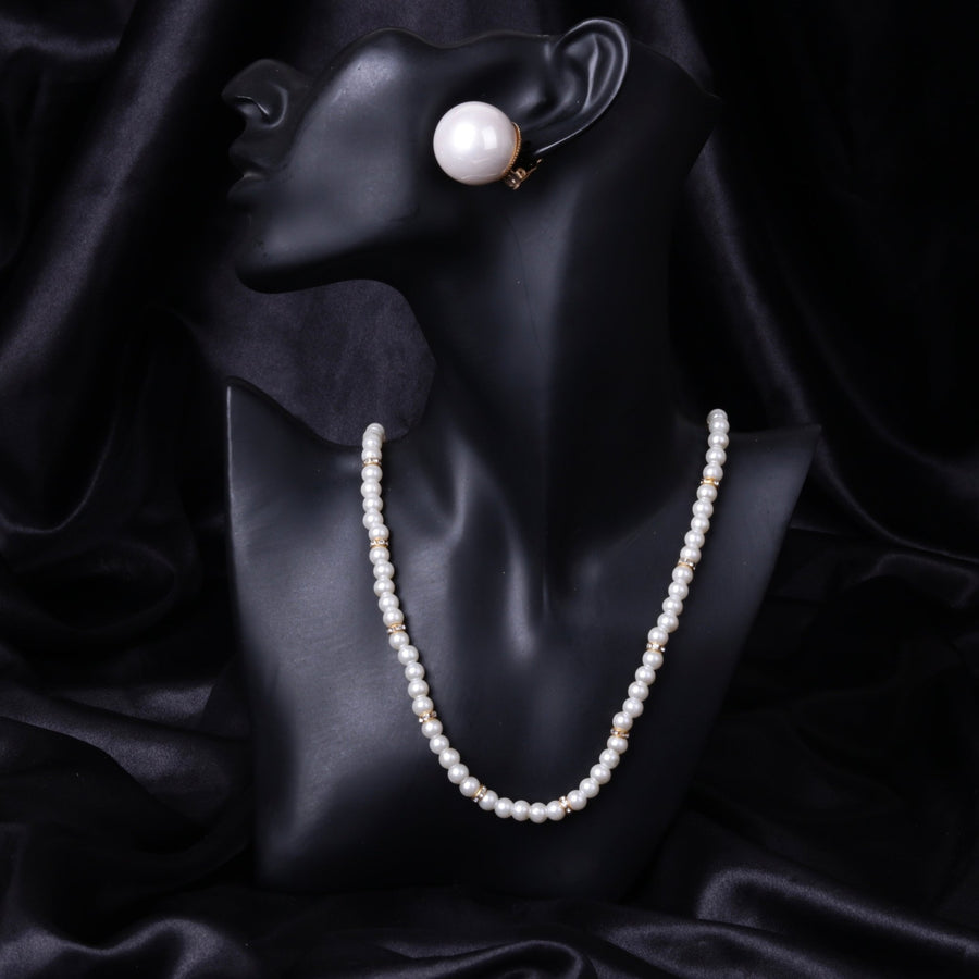 Black mannequin bust displaying a white mother of pearl necklace with gold-tone spacers and matching clip-on earring on a black satin background.