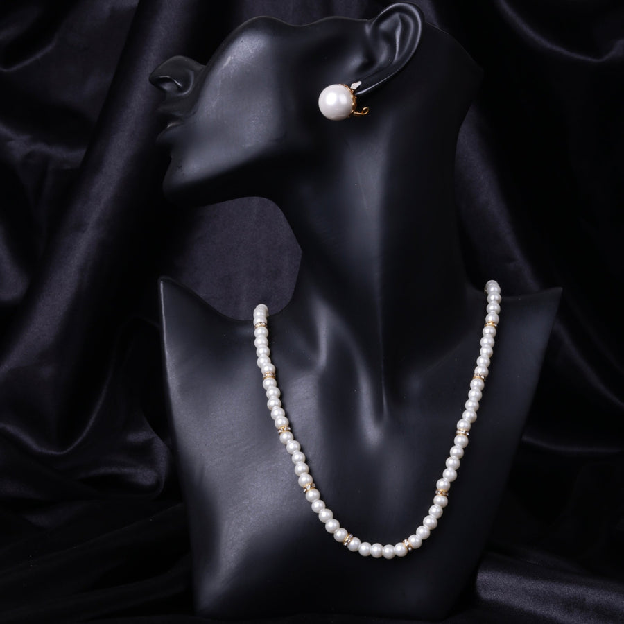Black mannequin bust with white pearl necklace and single matching clip-on mother of pearl earring against a black satin fabric background.