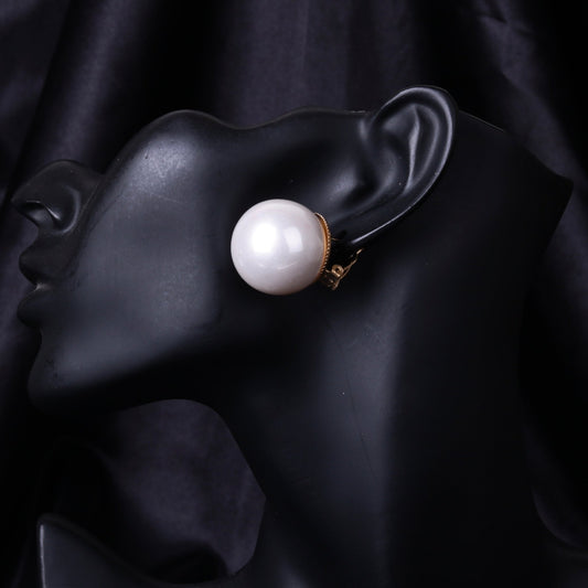 Close-up image of a black mannequin ear wearing a large white mother of pearl clip-on earring.