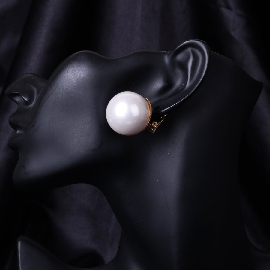 Close-up image of a black mannequin ear wearing a large white mother of pearl clip-on earring.