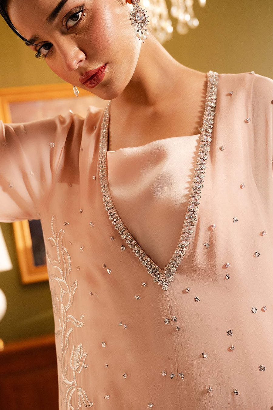 Close-up of deep V-neckline embellished with crystals and tiny scattered bead details on blush pink chiffon fabric
