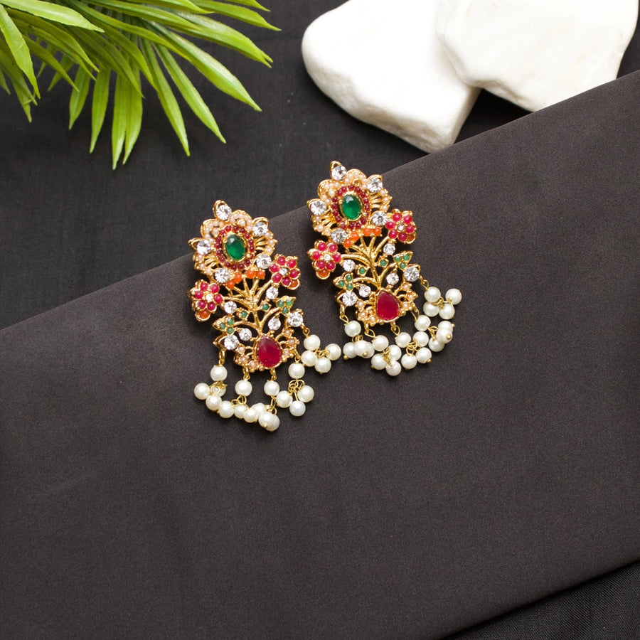 Gold-tone floral drop earrings with green, red, and coral stones accented by dangling pearl beads on a dark fabric background