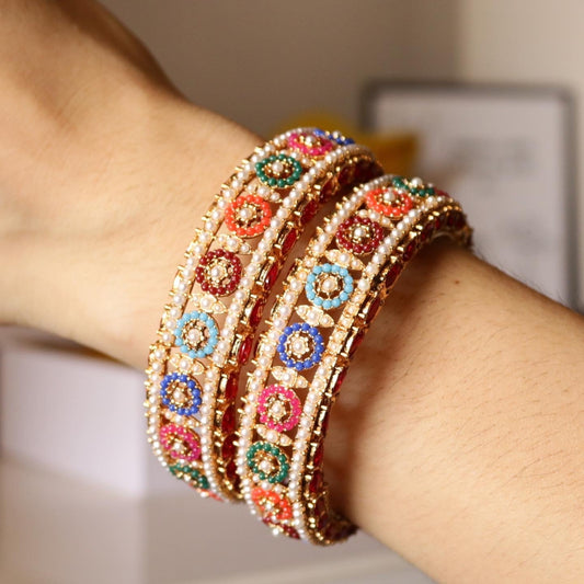 Close-up of colorful gold-plated bangles with pearl detail worn on a wrist, highlighting the vibrant hues and traditional design