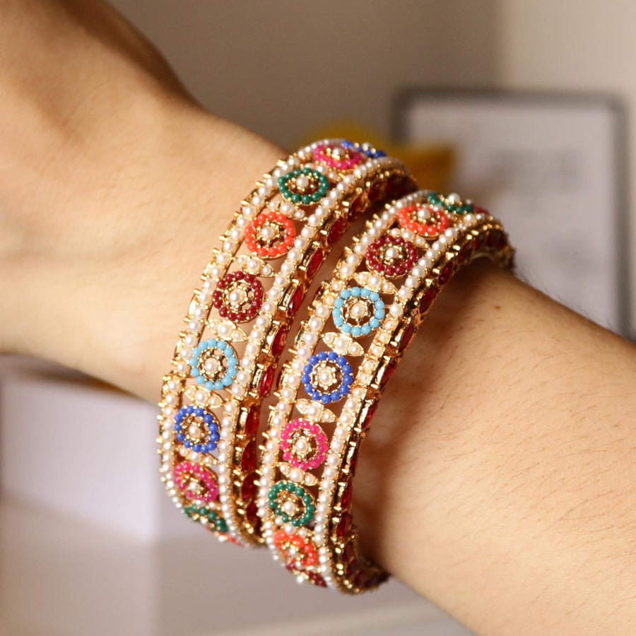 Close-up of colorful gold-plated bangles with pearl detail worn on a wrist, highlighting the vibrant hues and traditional design