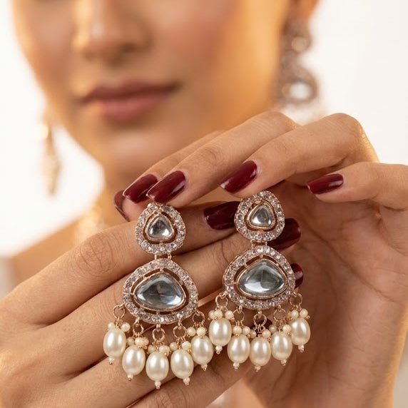 Hands holding a pair of Noor Polki drop earrings, highlighting intricate stonework and pearl detailing with polished nails