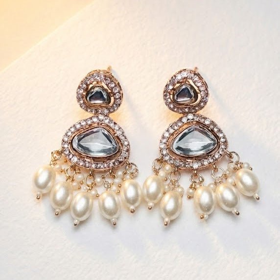 Close-up view of Noor Polki drop earrings on a textured light surface showcasing sparkling stones and cluster of pearl drops