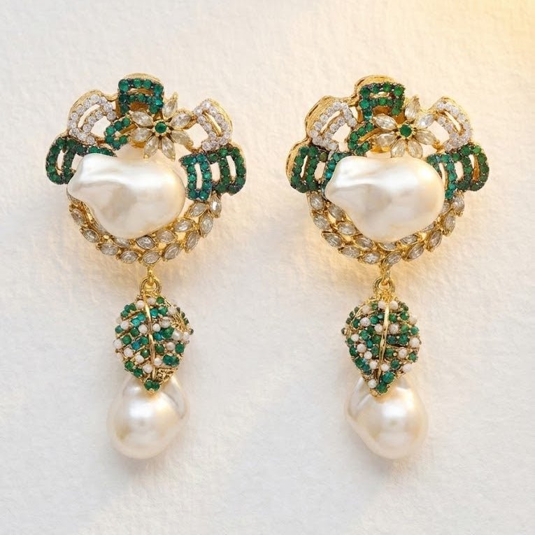 Emerald green and white pearl drop earrings displayed on textured fabric