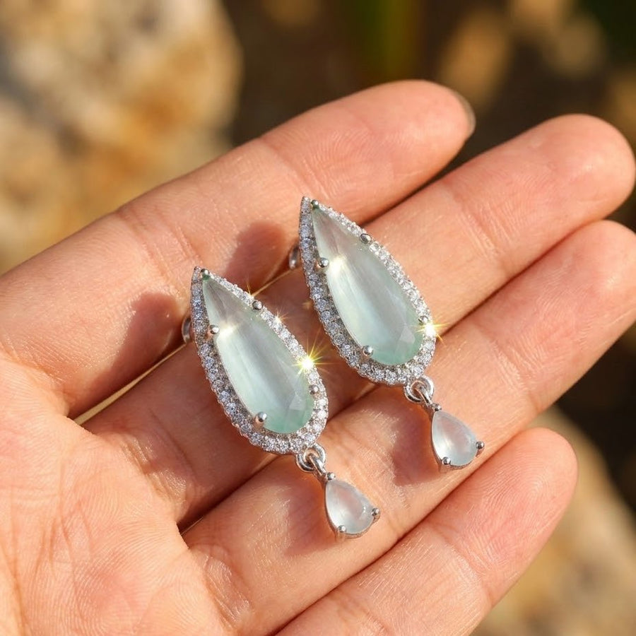 Blue teardrop crystal earrings with smaller dangling stones held in hand outdoors in natural light
