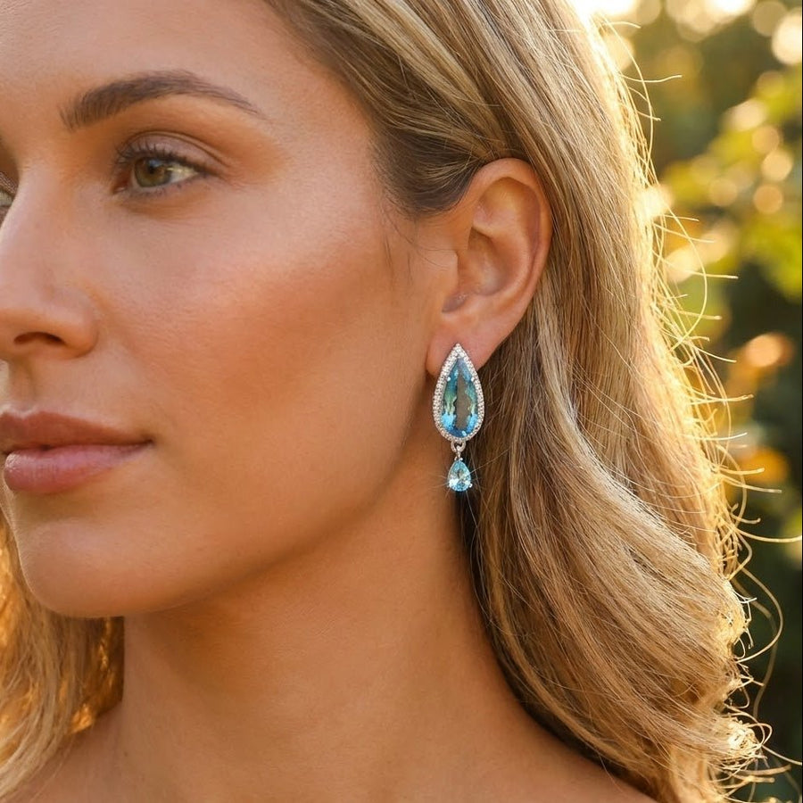 Close-up of woman with light hair wearing blue teardrop crystal earrings against green natural background
