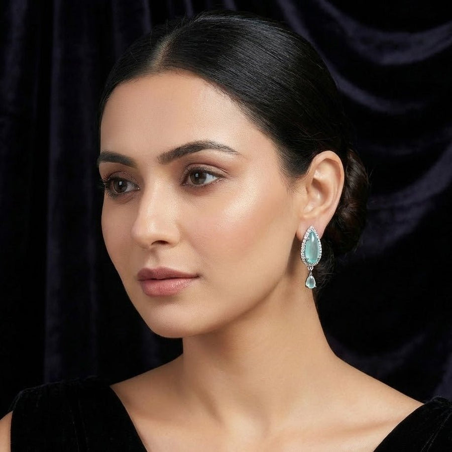 Model wearing pale aqua teardrop crystal earrings with neat updo and dark background