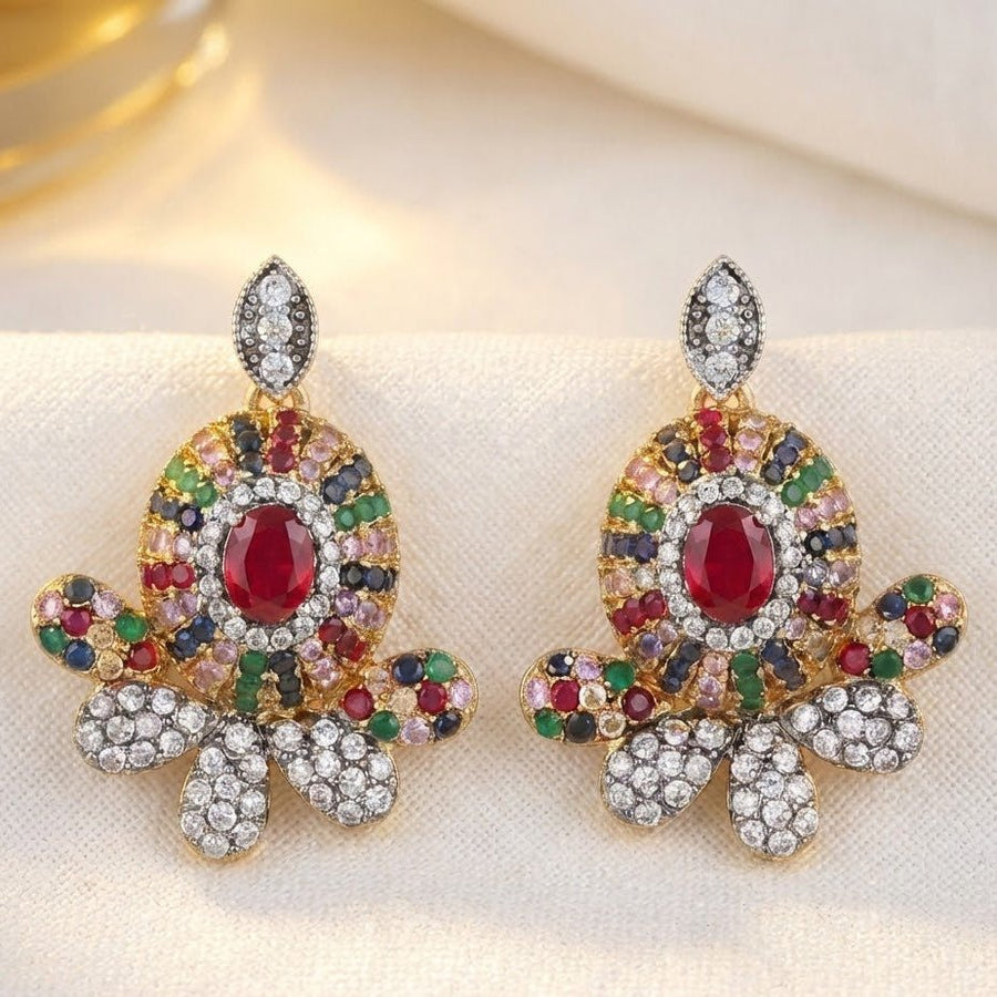 Ruby red central gemstone floral stud earrings with multicolor surrounding stones displayed on beige fabric