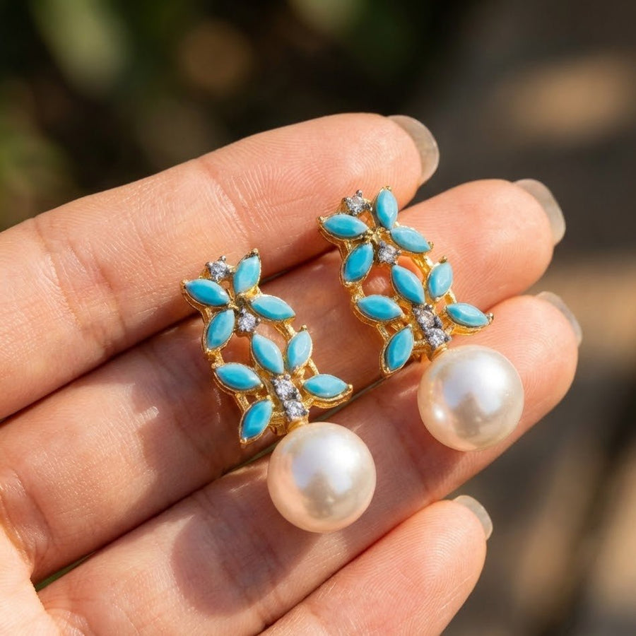 Elegant gold-tone drop earrings with pearl drops showcased on black textured surface