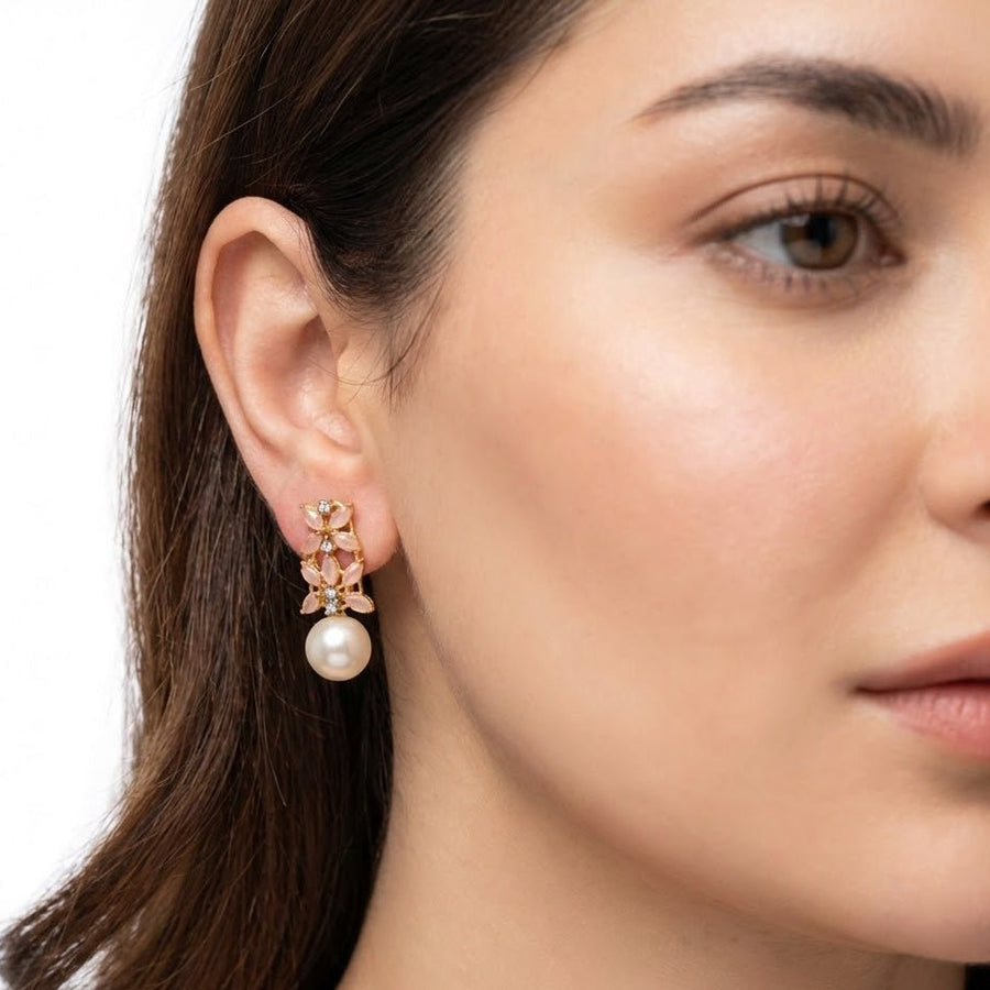 Hand holding pearl drop earrings with a mix of colorful stones against blurred outdoor background
