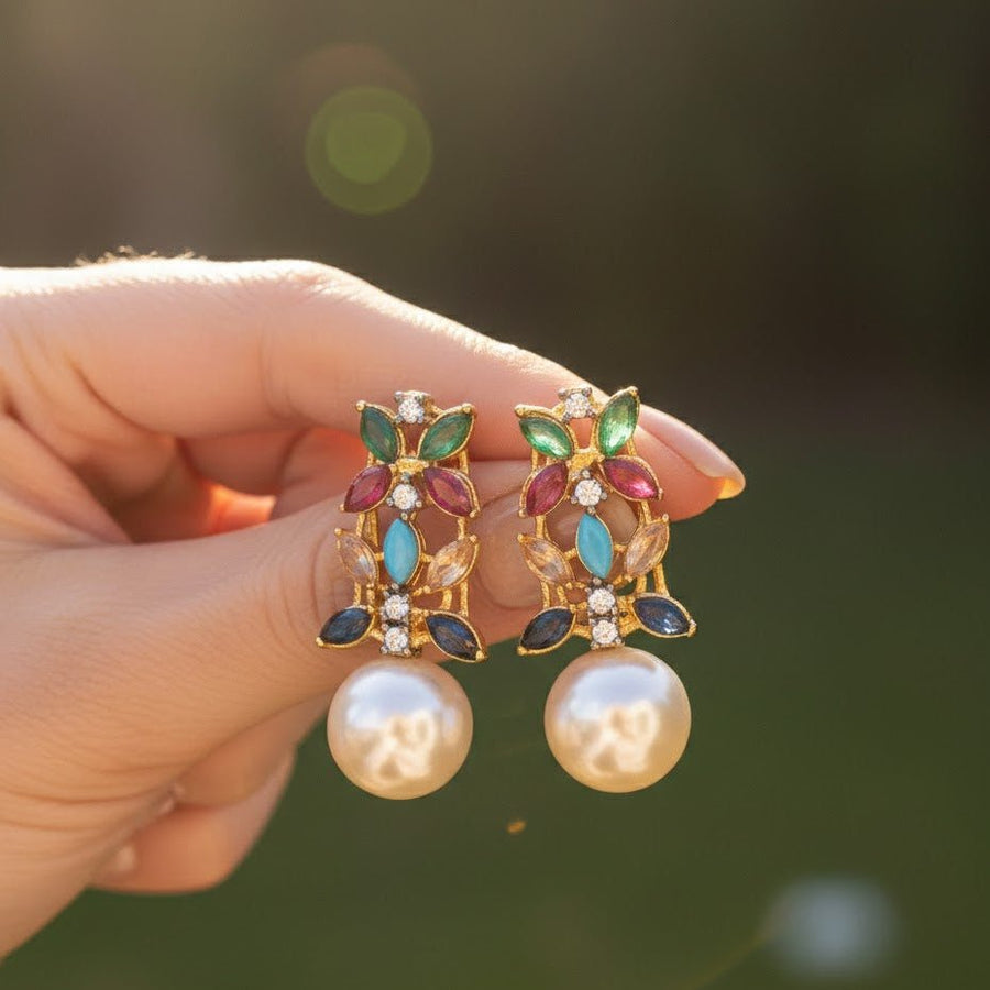 Hand holding multicolor pearl drop earrings against blurred green outdoor background showing color details