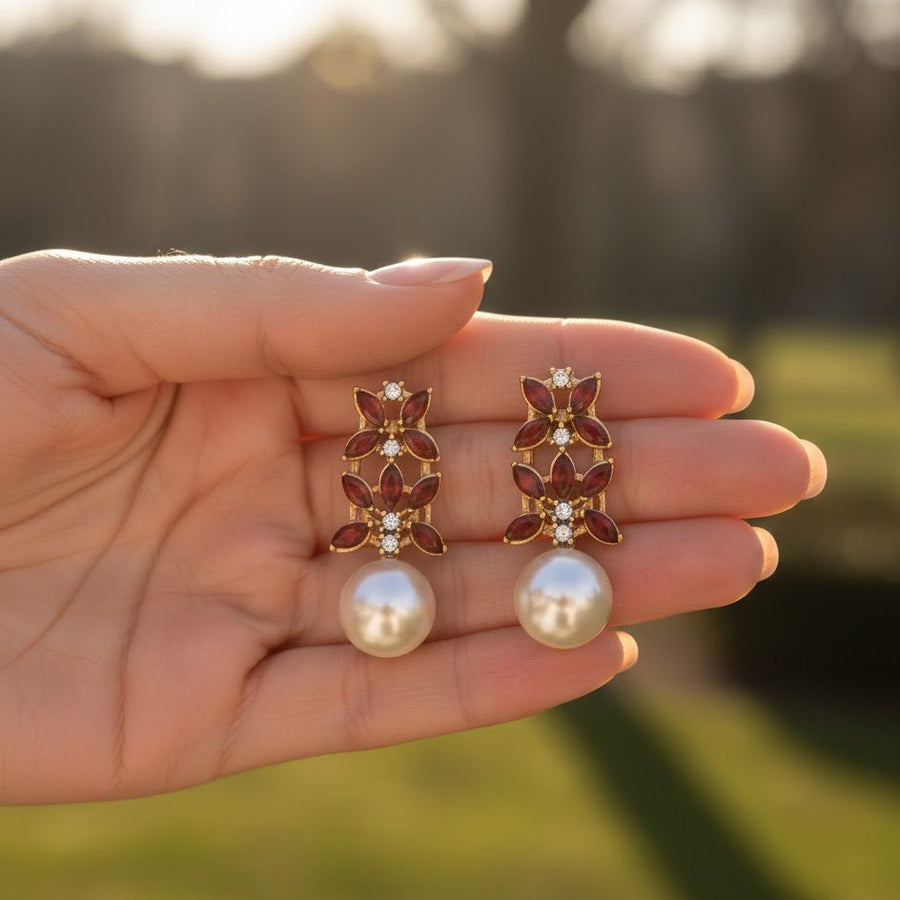 Person holding gold-tone red stone pearl drop earrings with clear color visibility