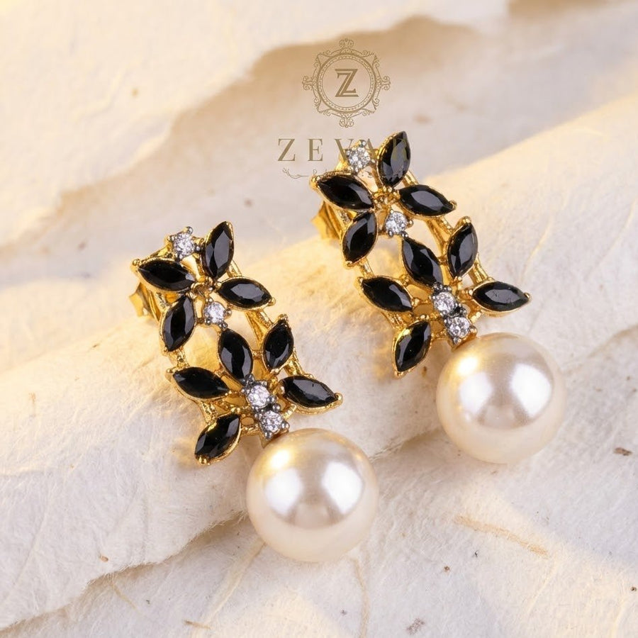 Black marquise stone pearl drop earrings displayed on beige textured surface with brand watermark