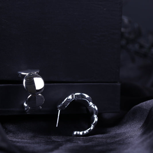 Silver chunky hoop earrings resting on black velvet with reflective polished surface