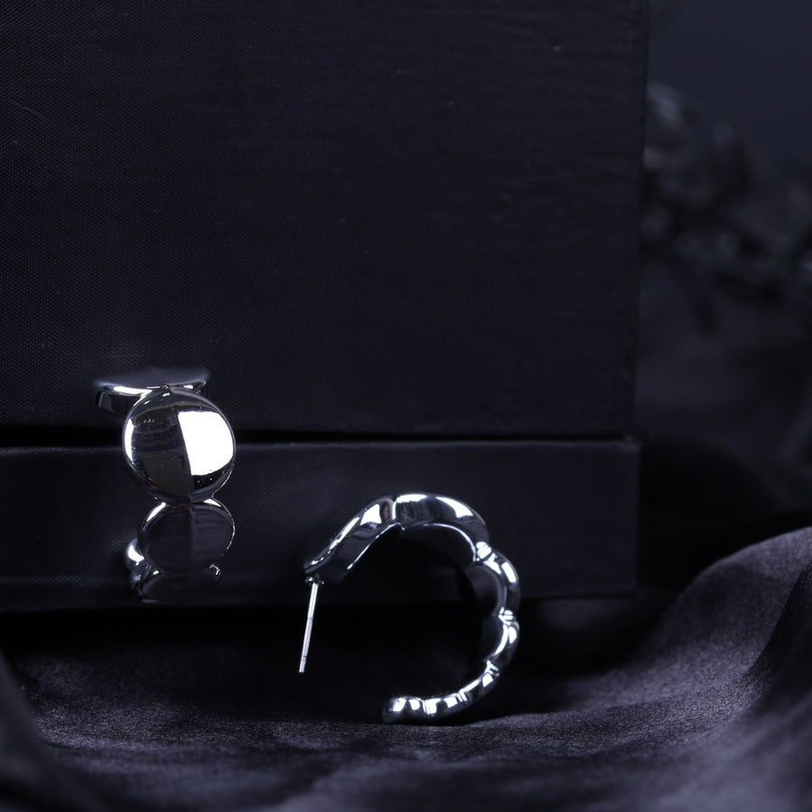 Silver chunky hoop earrings resting on black velvet with reflective polished surface
