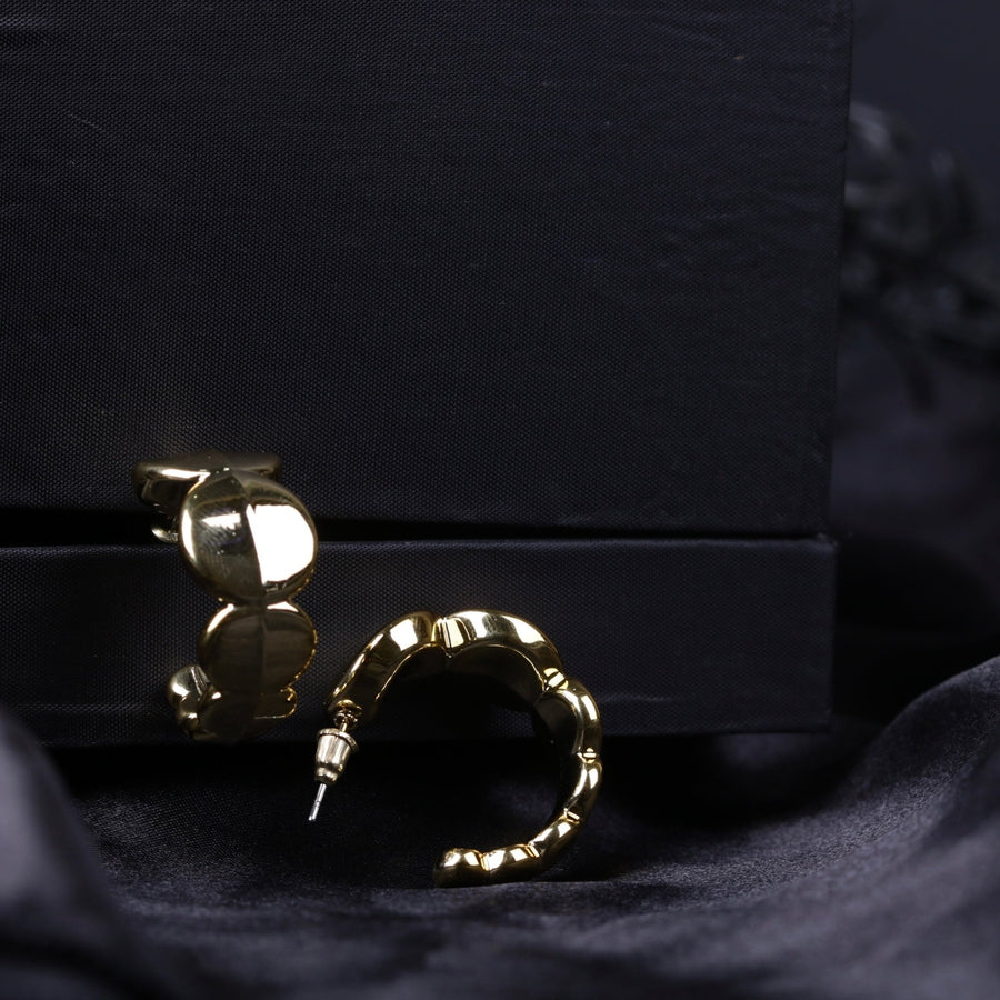 Pair of gold chunky hoop earrings lying on black velvet next to black box, showcasing shine and texture