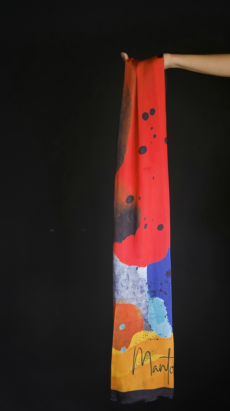 Hand holding a long scarf with vibrant abstract color splashes in red, black, blue, orange, and yellow on a black background