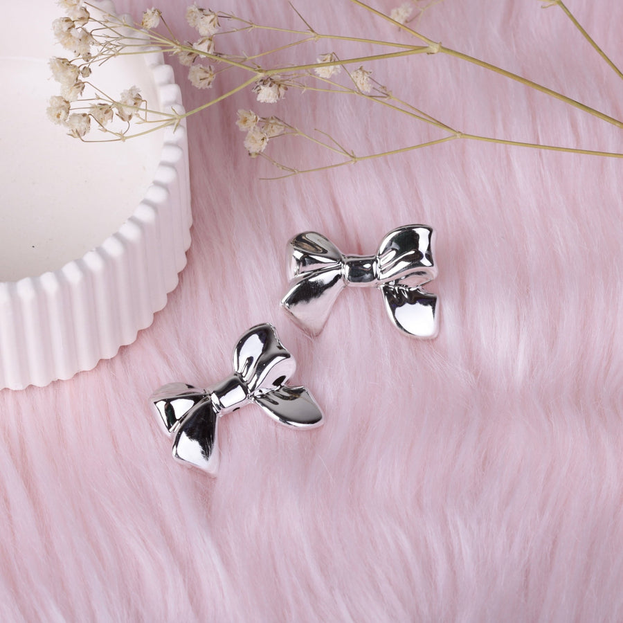 Pair of polished silver bow stud earrings on soft pink faux fur background with decorative dried flowers