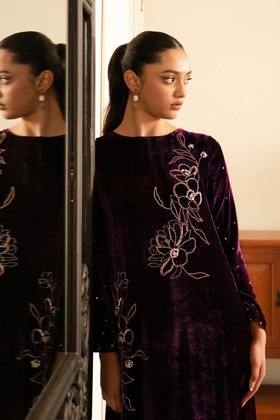 Close-up of jewelry and floral embroidery detail on the deep purple velvet dress showing intricate design.