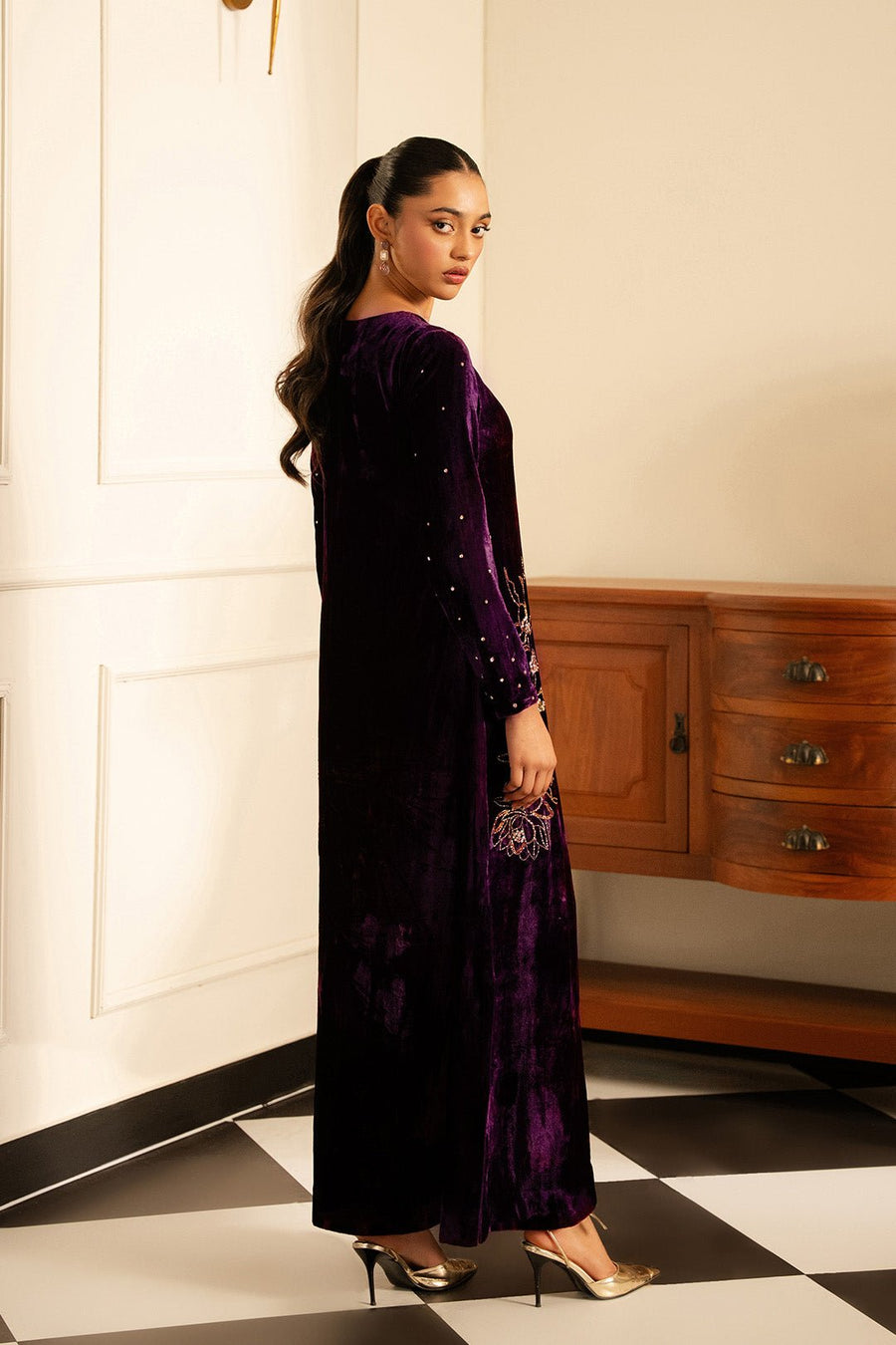 Back-side angled view of model in deep purple velvet dress highlighting its elegant modest design and embroidery.