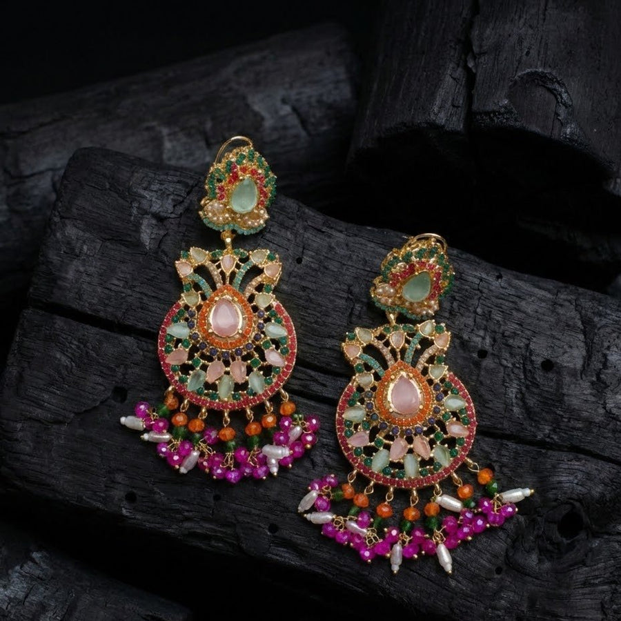 Woman holding a pair of pink and green gemstone embellished jhumka earrings with pearl dangles, showcasing detailed craftsmanship