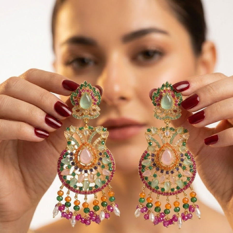 Pink and green multi-gemstone jhumka earrings displayed on dark wood background showing intricate detailing and bright pearl accents
