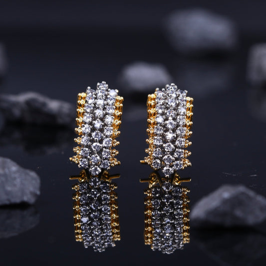 Close-up view of a pair of gold-plated stud earrings adorned with multiple rows of sparkling American zirconia stones on a reflective black surface with dark stones in background