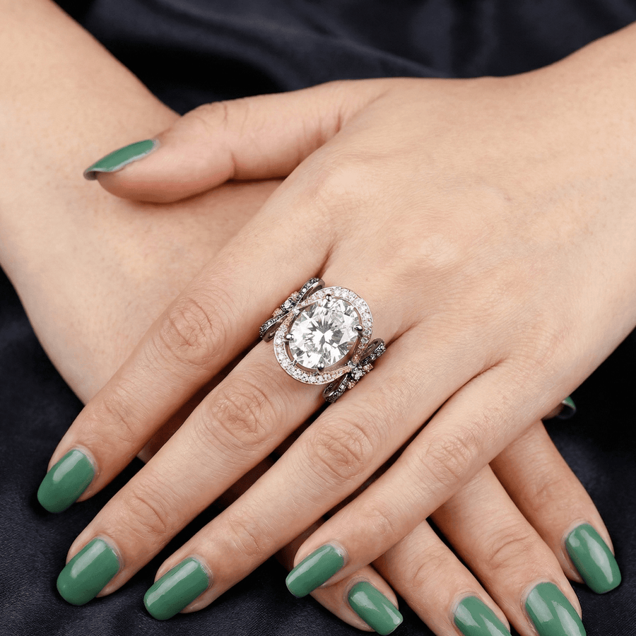 Model wearing a rose gold ring with a large oval clear gemstone set within halo stones and black oxidized bow side details