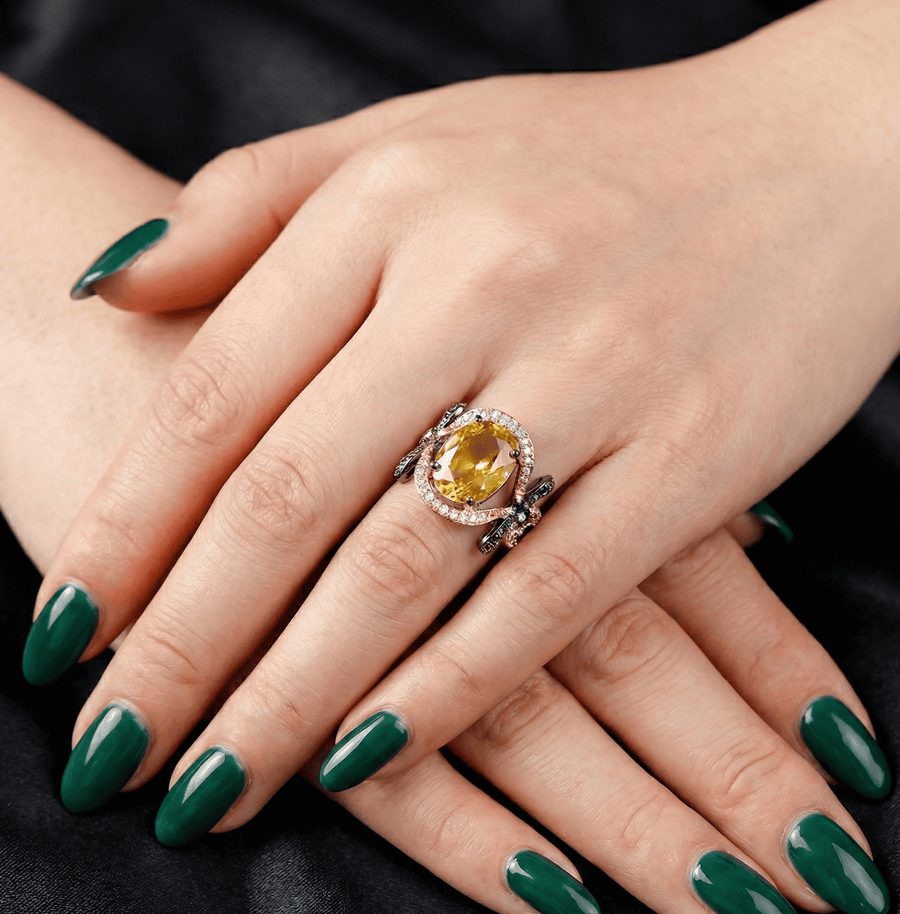 Model wearing the rose gold ring featuring a large oval yellow gemstone centerpiece accented by halo stones and black oxidized bows