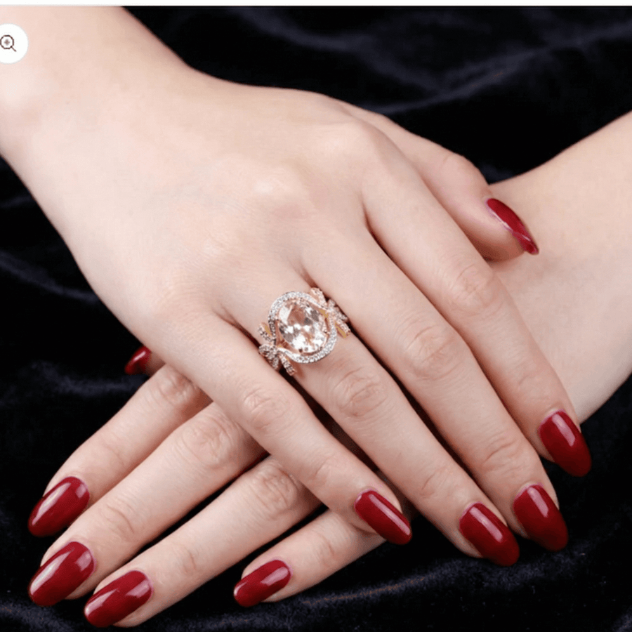 Pink semi-precious gemstone bow ring on a woman’s hand with red manicure on a black velvet background